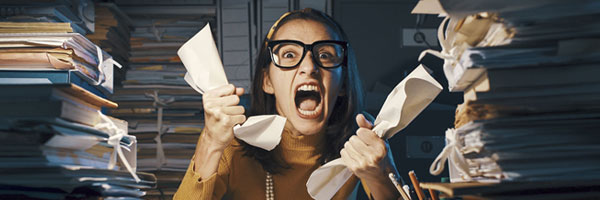 Woman stressed at desk holding papers and yelling.